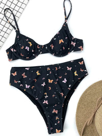 Bikini taille haute à armatures imprimé papillons noir posé à plat avec un chapeau de paille