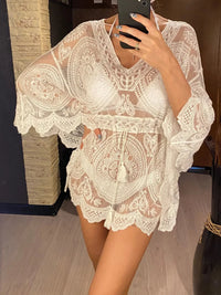 Tunique de plage blanche en dentelle à manches évasées portée de face par une femme qui se photographie, lien à la taille à pompons