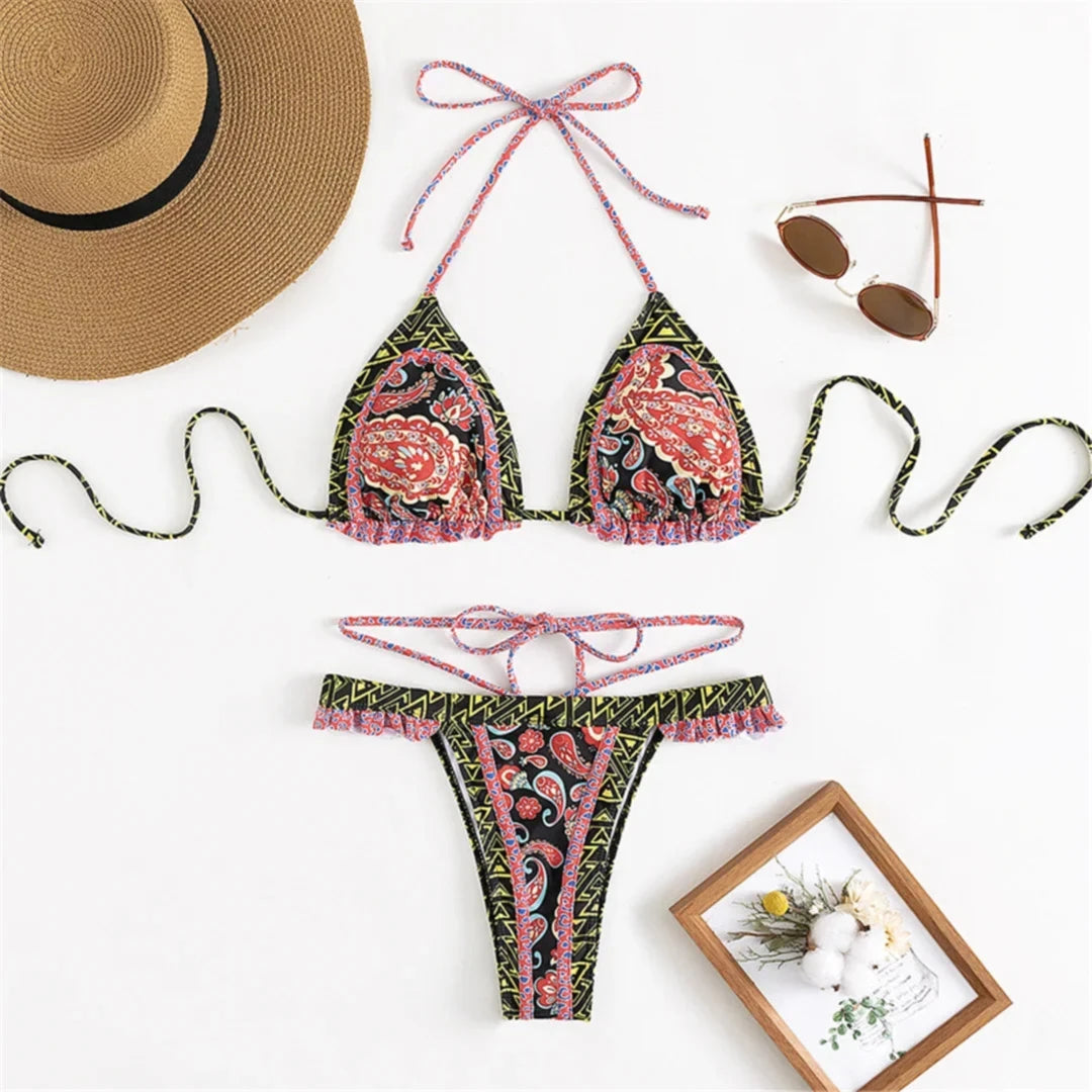 Bikini imprimé noir et rose à motifs paisley posé à plat avec un chapeau de paille, bas à cordons et volants roses