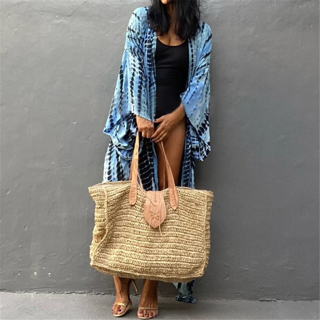 Tunique de plage imprimée manches longues à ceinture bleu portée de face, grand sac en paille et haut noir dessous