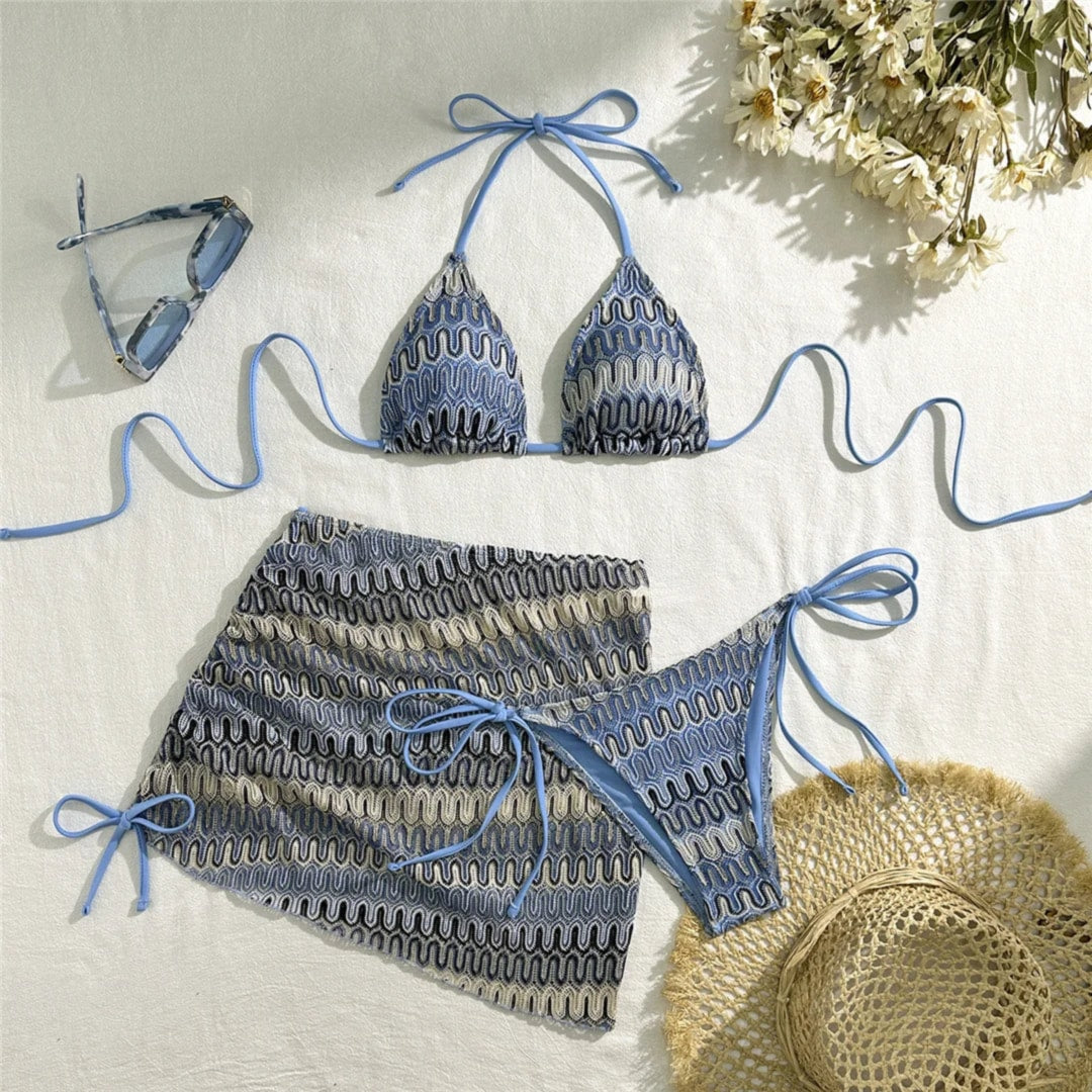Maillot trois pièces imprimé bleu posé à plat sur un tissu blanc, haut à lanières bleues, bas et jupe assortis