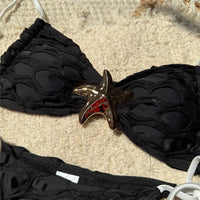 Gros plan sur l'étoile métal du bikini noir échancré, bonnet texturé en relief et lanières blanches