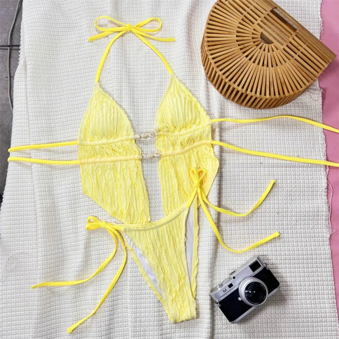 Tankini col halter texturé bas échancré jaune posé à plat avec sac en bambou et appareil photo, liens longs et perles