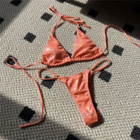 Bikini brillant scintillant triangle taille basse orange posé à plat sur un tapis, liens longs et culotte fine à anneau