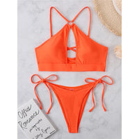 Bikini tour de cou à découpes et lanières orange posé à plat sur marbre, haut à découpe croisée et bas à lanières