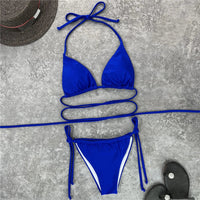 Bikini brésilien bleu roi étalé à plat sur un béton gris avec un chapeau de paille et des sandales noires