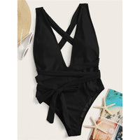 Maillot de bain une pièce triangle croisé noir posé à plat à côté d'un chapeau de paille et de sandales blanches