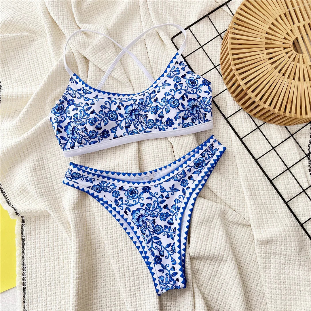 Bikini brésilien triangle imprimé bleu et blanc posé à plat sur tissu crème, liseré bleu festonné sur le bas