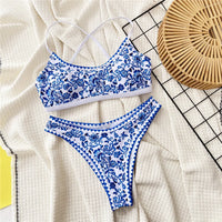 Bikini brésilien triangle imprimé bleu et blanc posé à plat sur tissu crème, liseré bleu festonné sur le bas