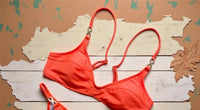 Gros plan sur le haut du bikini triangle à anneaux dorés et bretelles fines orange corail