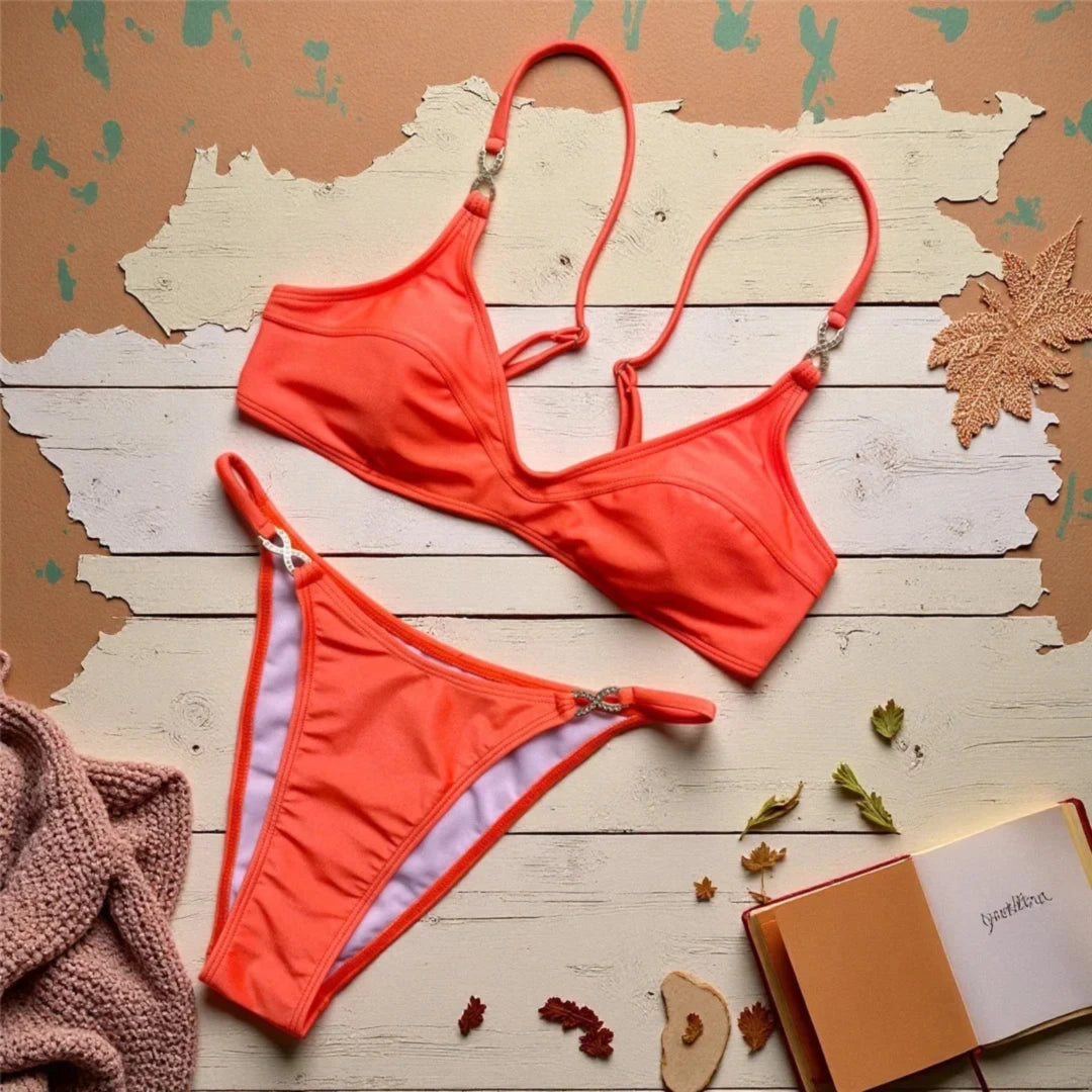Bikini triangle orange décolleté en V orné de strass posé à plat sur bois peint, feuilles mortes et carnet autour