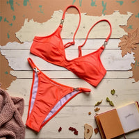 Bikini triangle orange décolleté en V orné de strass posé à plat sur bois peint, feuilles mortes et carnet autour
