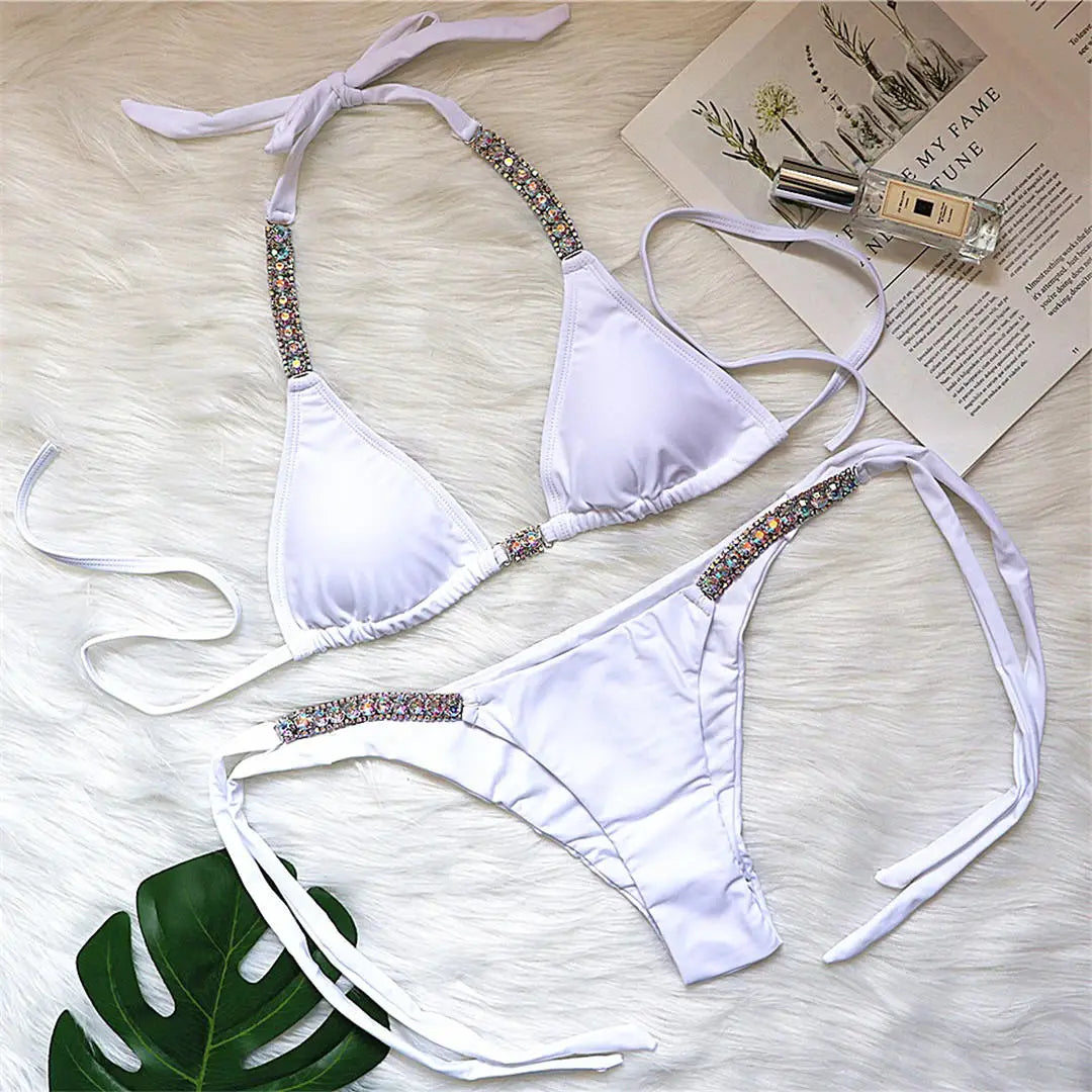 Bikini orné de strass brillants taille basse blanc posé à plat sur une fourrure blanche, feuille verte et magazine