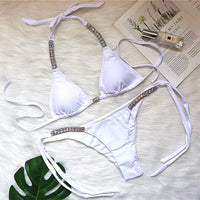 Bikini orné de strass brillants taille basse blanc posé à plat sur une fourrure blanche, feuille verte et magazine