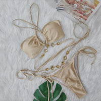Bikini croisé sans armatures orné de strass camel posé à plat sur fourrure blanche, feuille verte et chaîne de pierres dorées