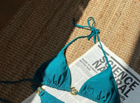 Gros plan sur le haut du bikini triangle à anneaux dorés et bas échancré bleu canard