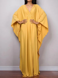 Robe de plage longue kaftan manches chauve-souris jaune portée de face en plan large, manches déployées et tissu fluide