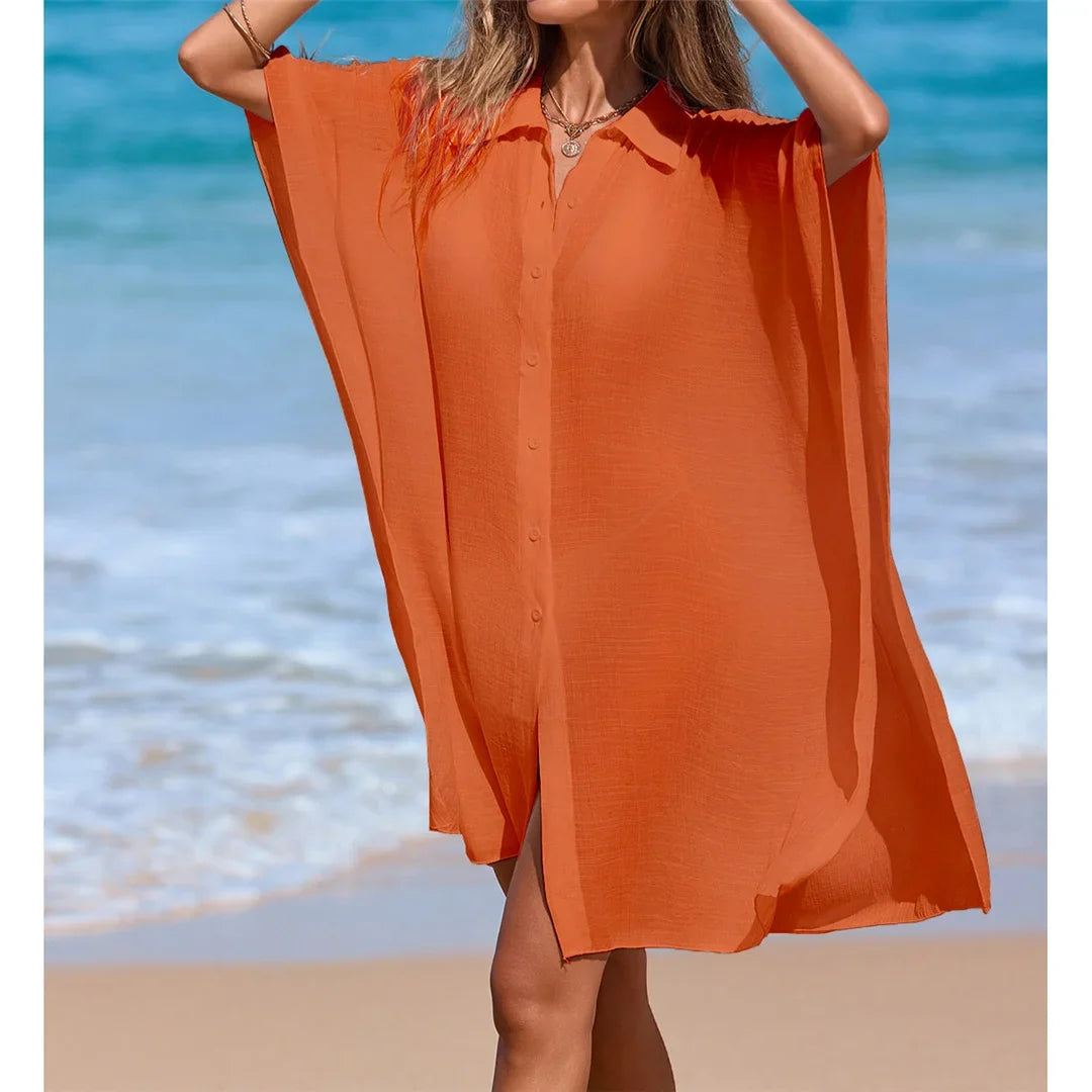 Chemise de plage longue à manches courtes en maille orange portée de face, mains relevées dans les cheveux sur la plage