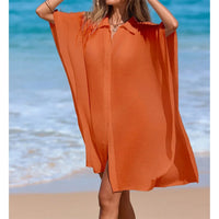 Chemise de plage longue à manches courtes en maille orange portée de face, mains relevées dans les cheveux sur la plage