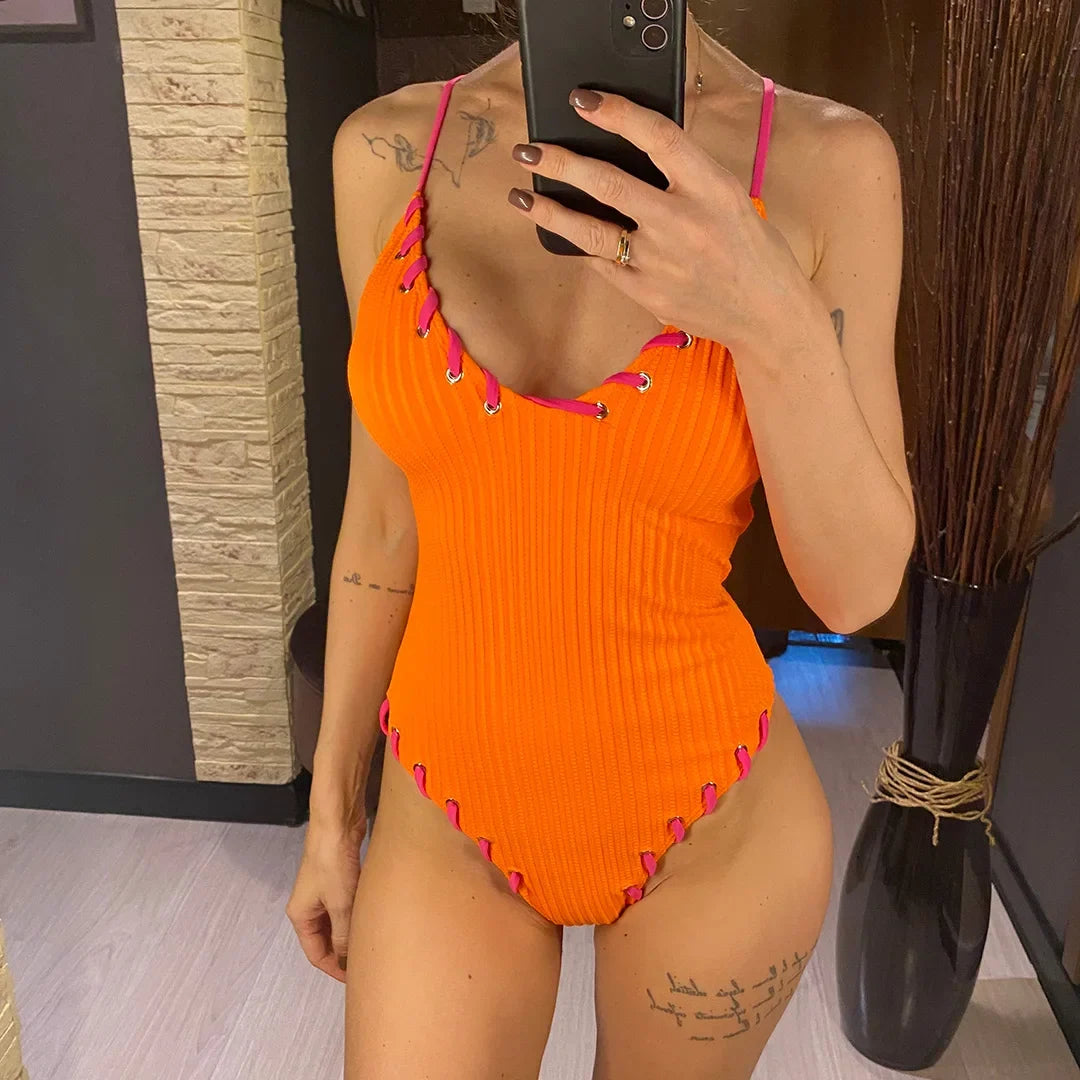 Maillot de bain une pièce côtelé orange porté de face, mains sur les hanches, bordures lacées fuchsia au col v