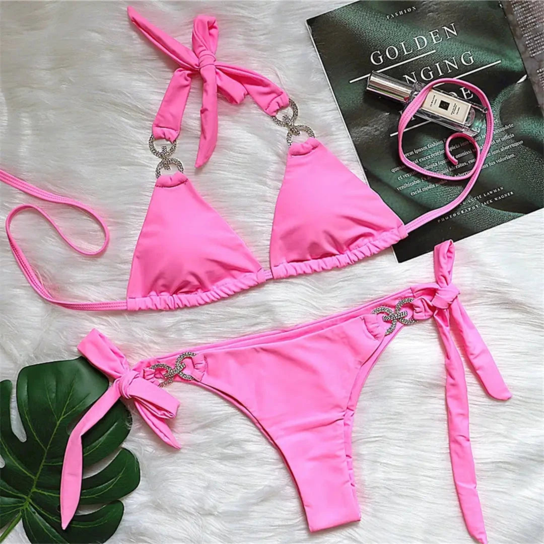 Bikini brésilien tour de cou à ornements strass rose posé à plat sur une fourrure blanche, près d'un magazine