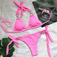 Bikini brésilien tour de cou à ornements strass rose posé à plat sur une fourrure blanche, près d'un magazine