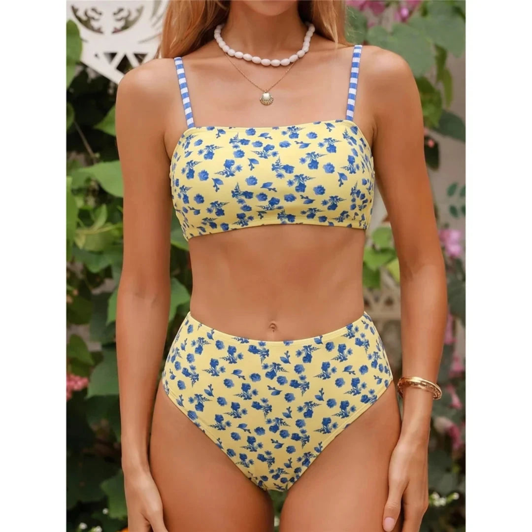 Bikini jaune clair à fleurs bleues porté de face par une femme devant une haie fleurie, perles au cou, taille haute