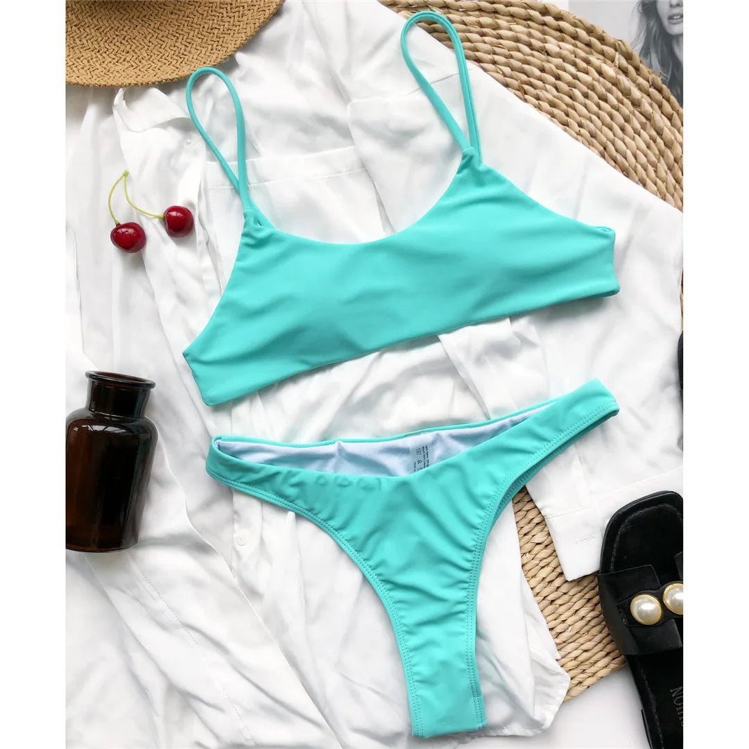 Bikini string brassière vert d'eau posé à plat sur une chemise blanche, à côté de cerises et d'une bouteille