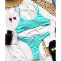 Bikini string brassière vert d'eau posé à plat sur une chemise blanche, à côté de cerises et d'une bouteille