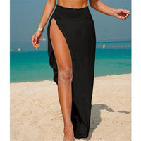 Jupe de plage noire à taille élastiquée et fente haute, portée de face sur une plage ensoleillée