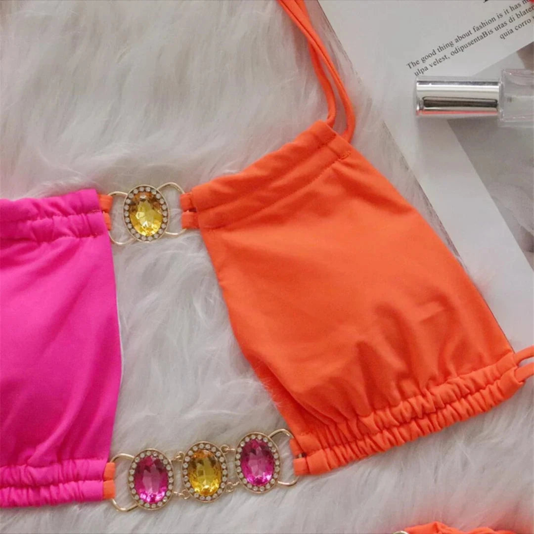 Gros plan sur le haut rose fuchsia et orange, anneaux dorés ornés de pierres jaunes et roses entre les deux couleurs du bikini