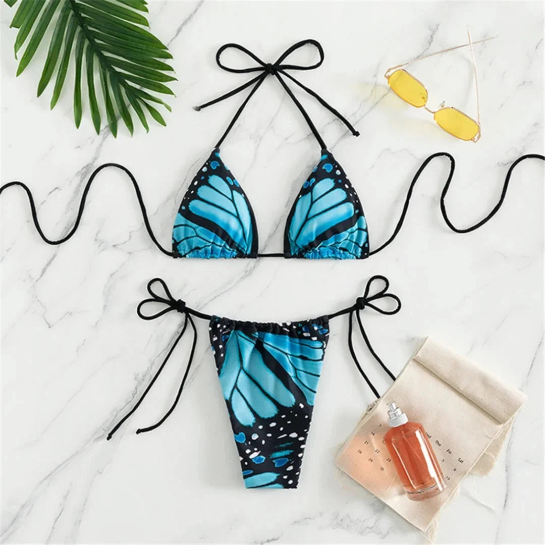 Maillot de bain deux pièces tour de cou imprimé bleu à ailes de papillon posé à plat sur marbre, liens noirs et haut triangulaire