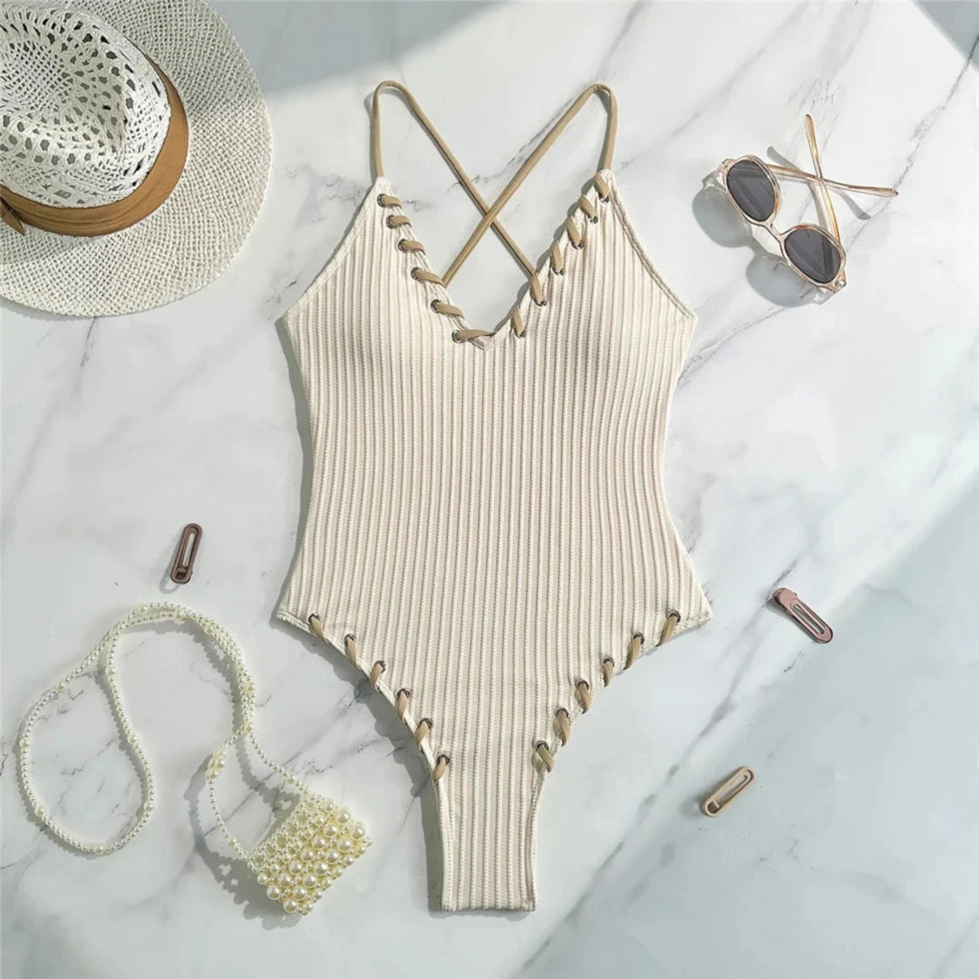 Maillot de bain une pièce côtelé beige posé à plat sur marbre avec accessoires de plage, bretelles croisées