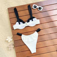 Bikini à armatures blanc à empiècements noirs à plat sur une planche de bois, avec lunettes de soleil et fleurs décoratives