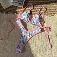 Bikini brésilien string taille basse imprimé fleuri rose posé à plat sur un tapis, liseré rose et liens latéraux longs