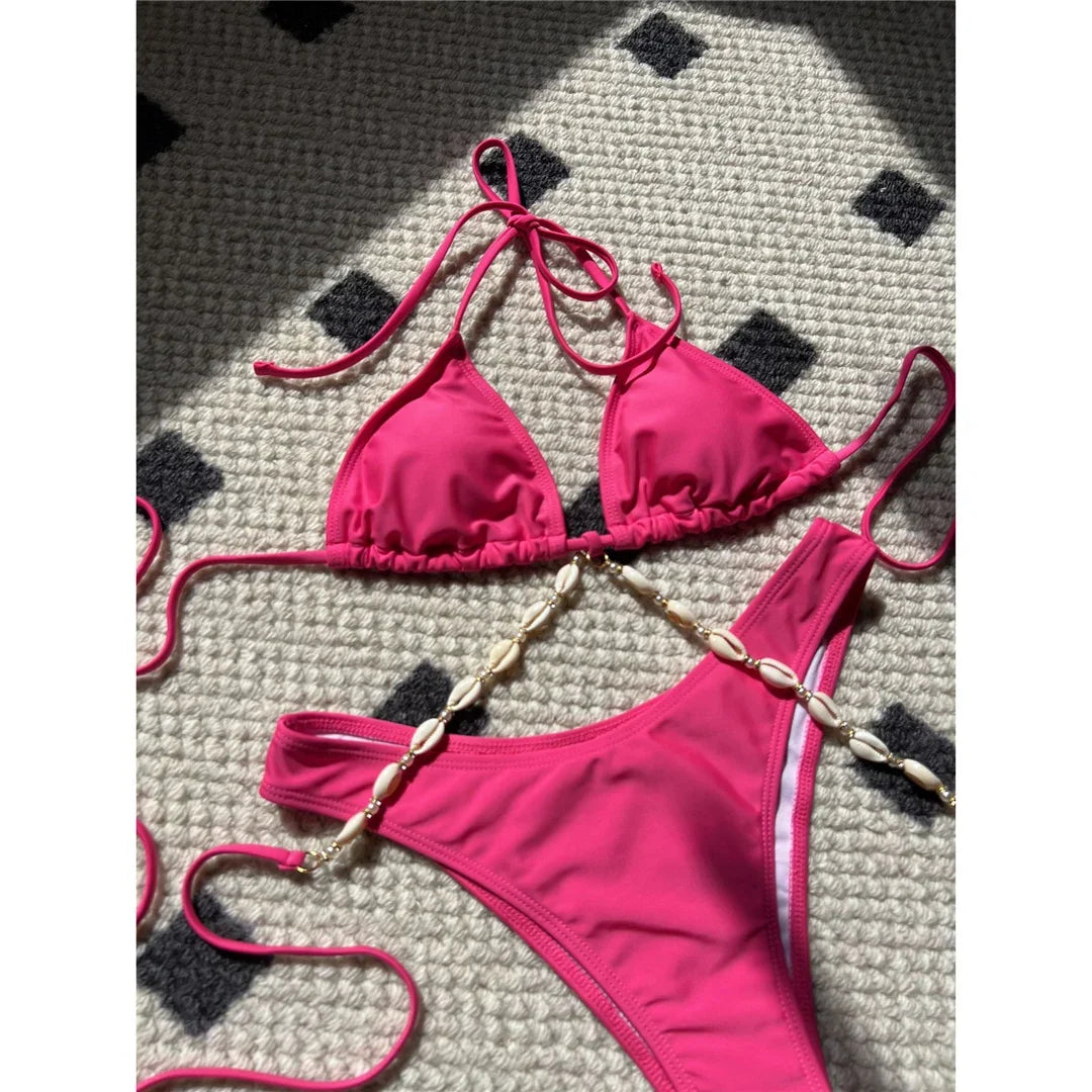 Gros plan sur la chaîne de coquilles dorées du bikini rose fuchsia, qui relie le triangle du haut au bas échancré