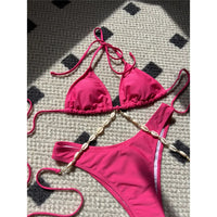 Gros plan sur la chaîne de coquilles dorées du bikini rose fuchsia, qui relie le triangle du haut au bas échancré