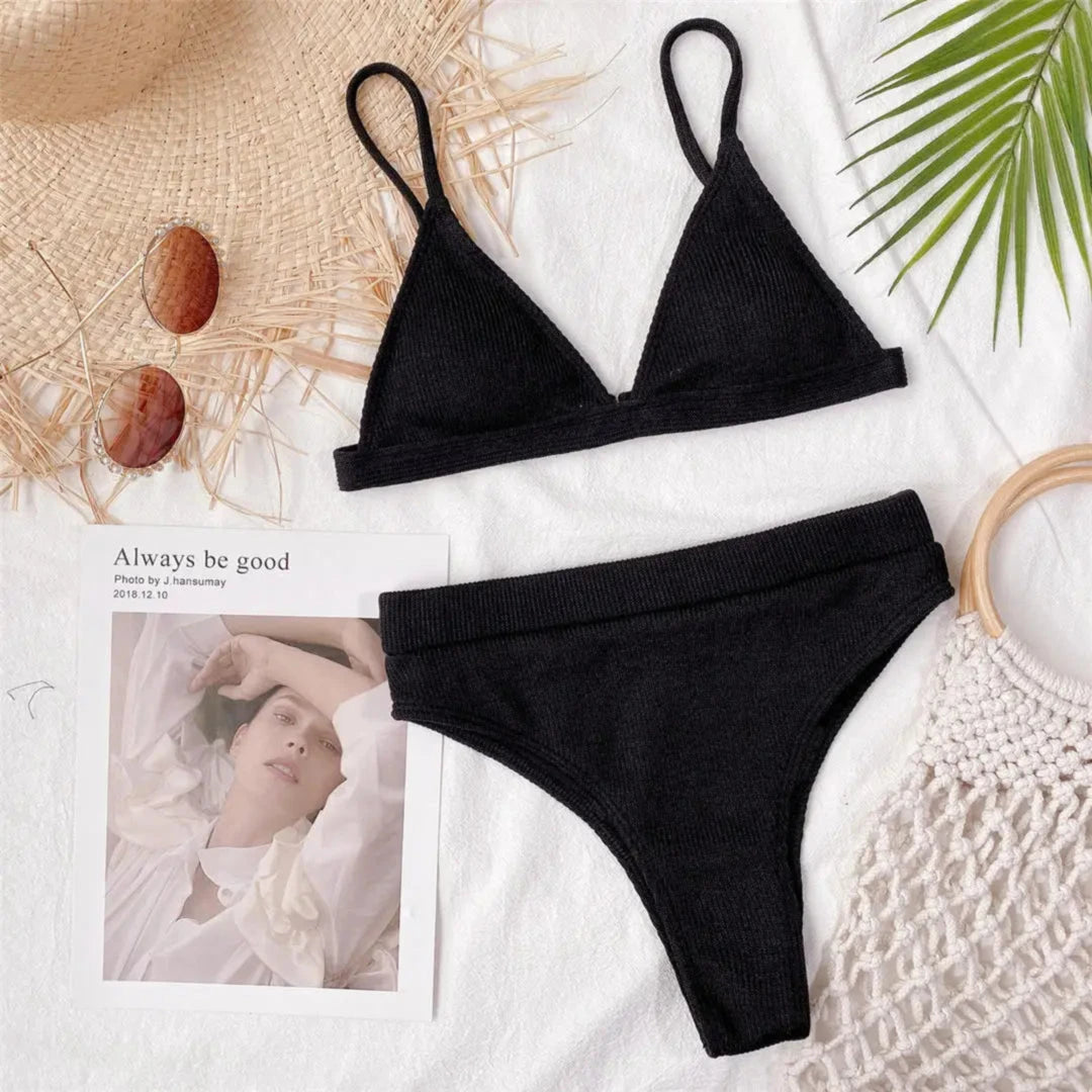 Bikini taille haute côtelé sans armatures noir posé à plat sur un magazine et un sac en osier