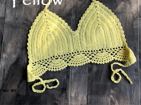 Haut de maillot de bain crochet tricoté jaune posé à plat sur du bois foncé, bretelles longues et bordure festonnée