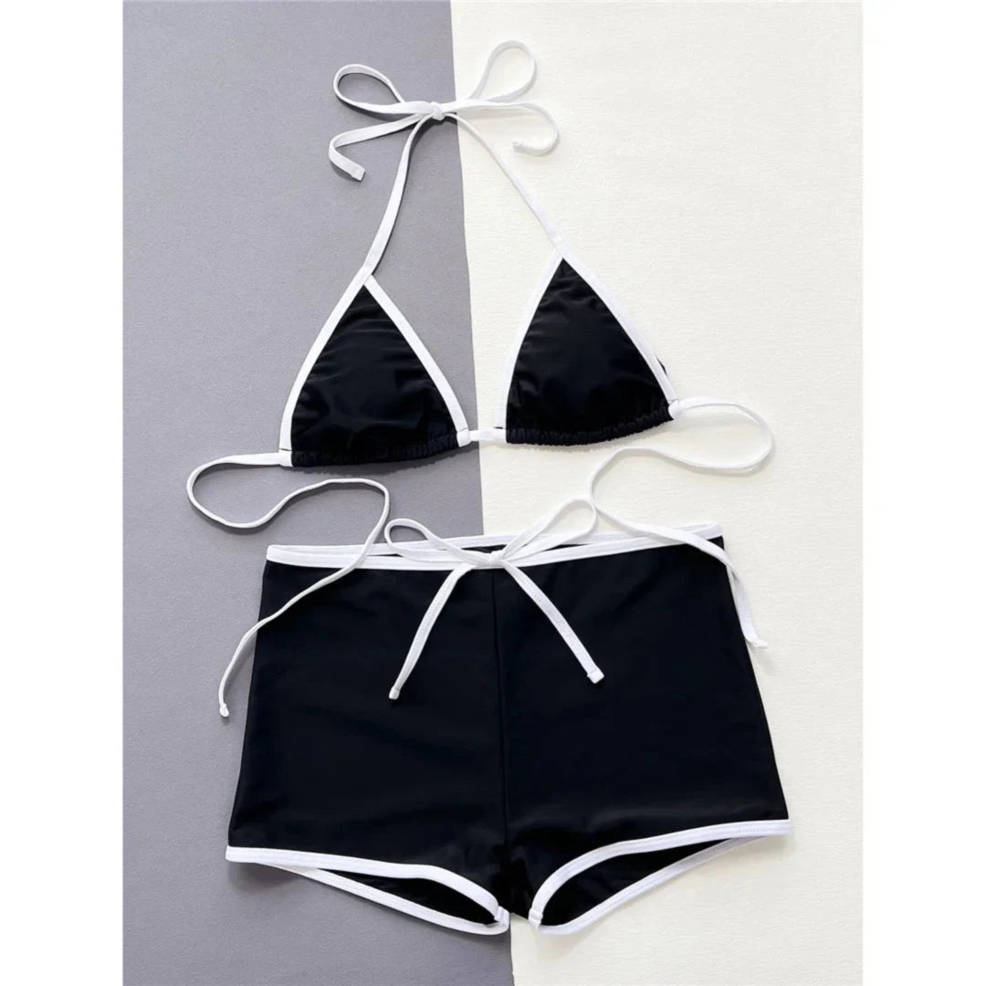 Bikini tour de cou noir à liseré blanc posé à plat sur fond bicolore, haut triangle et short à cordon blanc
