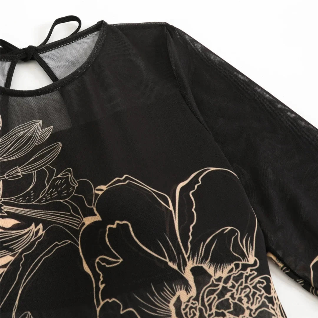 Gros plan sur l'épaule et la manche du body noir à fleurs au trait beige, encolure nouée d'un lien noir