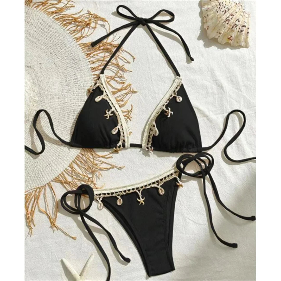 Bikini brésilien tour de cou patchwork à lanières noir posé à plat sur une nappe avec chapeau et coquillages