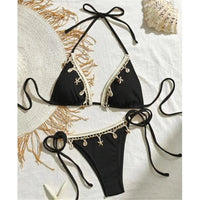 Bikini brésilien tour de cou patchwork à lanières noir posé à plat sur une nappe avec chapeau et coquillages