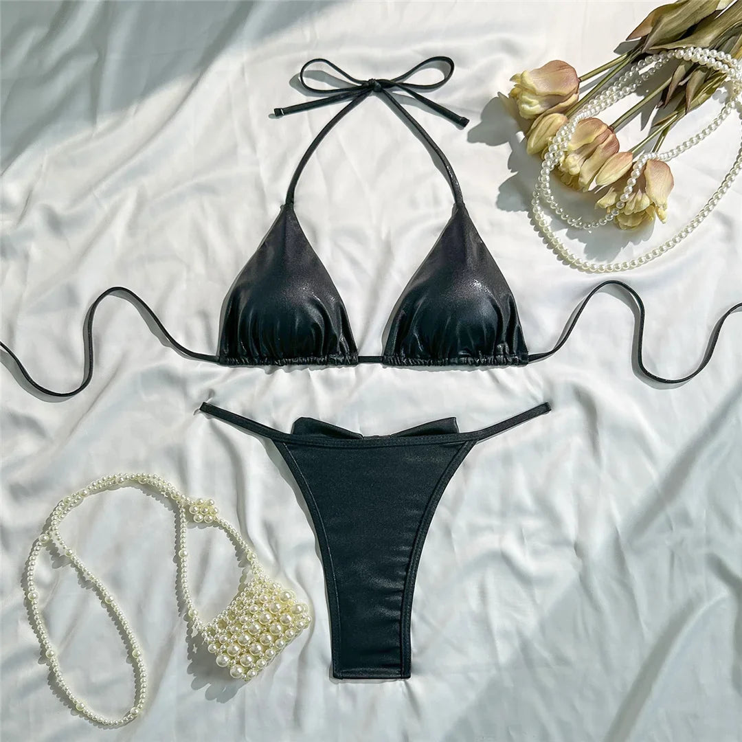 Bikini triangle tour de cou brillant noir posé à plat sur un tissu blanc, avec un sac en perles posé à côté