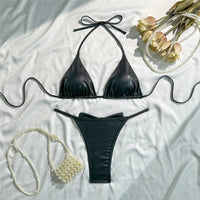 Bikini triangle tour de cou brillant noir posé à plat sur un tissu blanc, avec un sac en perles posé à côté