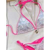 Gros plan sur le haut triangle blanc brillant à reflets irisés, bordure rose fuchsia et bouton de veste