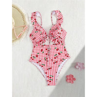 Maillot de bain une pièce échancré rouge à cerises posé à plat avec une fleur rose, volants aux bretelles