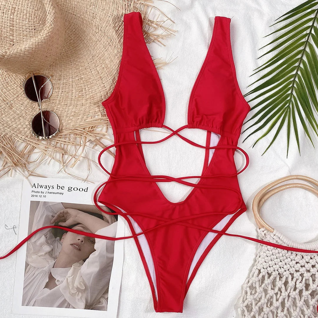 Monokini décolleté plongeant découpe ventre rouge posé à plat sur un tissu blanc, lanières croisées et chapeau de paille