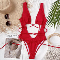 Monokini décolleté plongeant découpe ventre rouge posé à plat sur un tissu blanc, lanières croisées et chapeau de paille