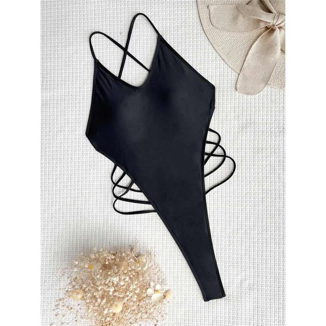 Maillot de bain une pièce noir posé à plat sur un tissu blanc, bretelles croisées et lanières sur les côtés
